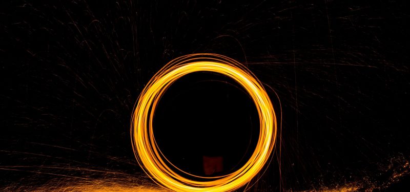 Burning steel wool being swirled in a circle at night to form a zero with slow exposure