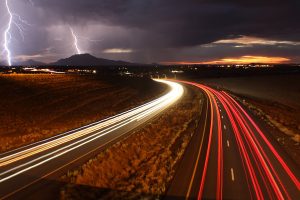 Long exposure shot of cars on the highway with lightning in the background
