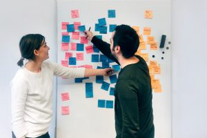 Two people collaborating on a whiteboard with sticky notes