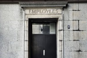 Photo of black wooden door in stone wall with employees craved into the lintal above door