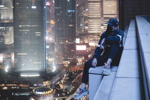 Livin' on the edge. Man sitting on building gutter at night surrounded by skyscrappers