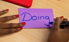 Person writing 'Doing' on a purple Post-it note