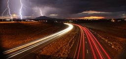Long exposure shot of cars on the highway with lightning in the background