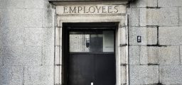 Photo of black wooden door in stone wall with employees craved into the lintal above door