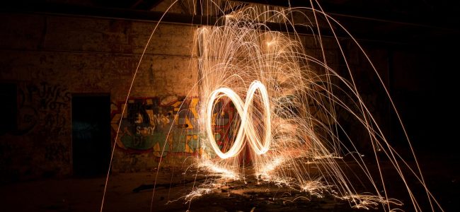 Long exposure nightime photograph of burning steel wool swung in an infinity pattern