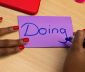 Person writing 'Doing' on a purple Post-it note