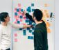 Two people collaborating on a whiteboard with sticky notes